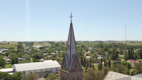 Orbital-close-up-of-a-romantic-style-church-tower-and-cross-with-Santa-Anita-town-and-Entre-Rios-countryside-in-background,-Argentina