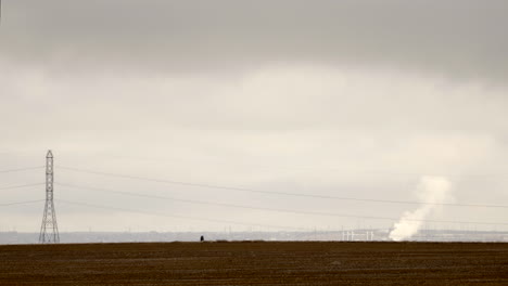 White-SUV-car-driving-left-to-right-on-rural-road-in-arid-farm-landscape-during-winter,-static-long-shot