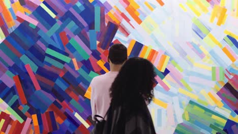 Man-Looking-At-The-Colorful-Wall-Painting-And-A-Woman-Crosses-By-Walking-Behind-Him---Medium-Shot