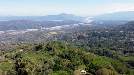 Aerial-rising-over-Jesus-Christ-statue,-large-river-and-mountain-ranges-in-vast-wilderness-landscape-in-remote-coffee-district-of-Ermera,-Timor-Leste,-Southeast-Asia