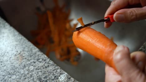 Woman-Peeling-The-Fresh-Carrot-On-The-Stainless-Kitchen-Sink---close-up,-selective-focus