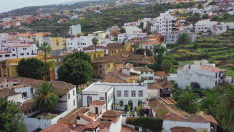 View-on-a-typical-spanish-town,-Icod-de-los-Vinos,-on-the-island-of-Tenerife,-Spain,-with-luxurious-mansions-and-villas,-parks-and-gardens,-exotic-palms-and-red-rooftops,-pedestal-aerial-shot-4K