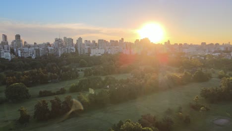 Aerial-dolly-out-of-Municipal-golf-course-in-Palermo-neighborhood-with-buildings-in-background-at-golden-hour,-Buenos-Aires
