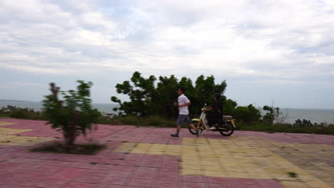 Side-shot-of-a-woman-riding-a-motorcycle-in-Vietnam-with-a-clear-view-of-the-ocean-in-the-background