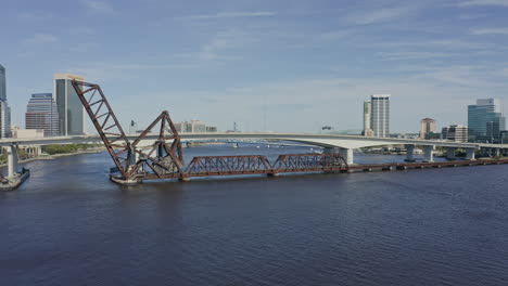 Jacksonville-Florida-Aerial-v8-pan-left-shot-of-railroad-bridge,-highway-bridge-and-traffic-during-rush-hour---March-2020