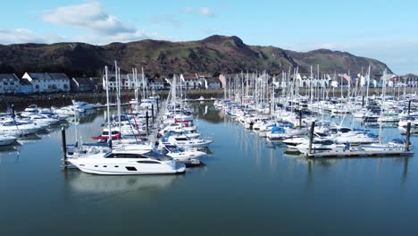 Luxury-yachts-and-sailboats-moored-in-Conwy-marina-mountain-waterfront-aerial-view-North-Wales-dolly-left-low