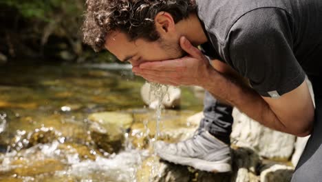 Bearded-male-traveler-washes-his-face-with-mountain-stream-water