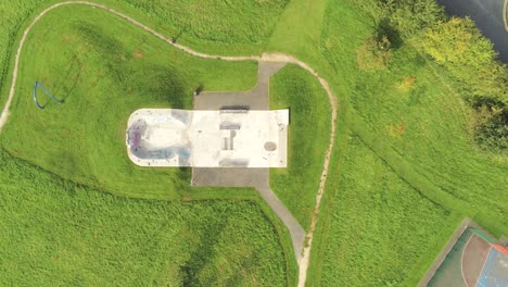 Public-skate-grassy-park-aerial-view-above-shaped-concrete-play-area-covered-in-graffiti