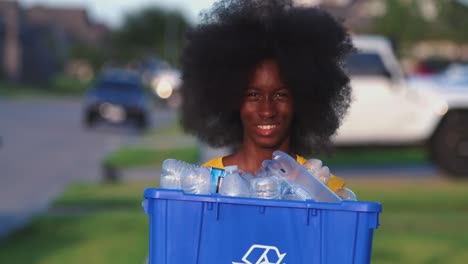 Adolescentes-Afroamericanos-Con-Una-Gran-Sonrisa-Afro-Mientras-Sostiene-Una-Papelera-De-Reciclaje-Llena-De-Botellas-De-Plástico