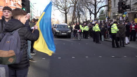 Ein-Junger-Mann-Schwenkt-Eine-Ukrainische-Flagge,-Während-Autos-An-Einer-Demonstration-Gegen-Die-Invasion-Der-Ukraine-Vor-Der-Russischen-Botschaft-Vorbeifahren