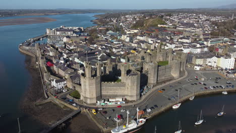 An-aerial-view-of-Caernarfon-Castle-on-a-sunny-day,-flying-right-to-left-around-the-castle,-Gwynedd,-North-Wales,-UK