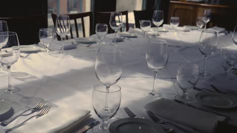 Dining-table-set-for-a-wedding-or-corporate-event-at-fine-dining-restaurant-ceramic-plates-forks-knives-cloth-napkins-on-white-tablecloth-on-table-Steady-Slow-motion-panning-up