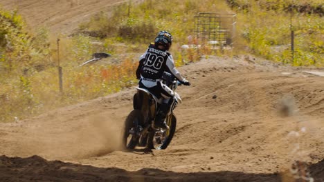 Female-motocross-driver-and-a-competitor-race-out-of-a-corner-in-slow-motion,-dirt-flying