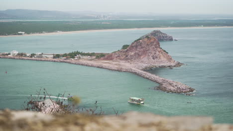A-tourist-boat-travels-the-pacific-ocean-in-Mazatlan,-Sinaloa-Mexico-with-mountains-and-beach-in-the-background