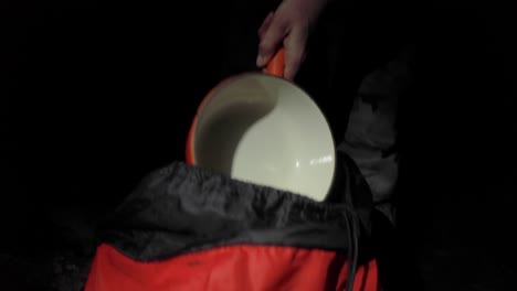 Slow-motion,-person-taking-cooking-pan-out-of-backpack-while-camping-at-night