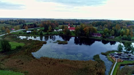 Aerial-backward-moving-shot-of-the-Āraiši-lake-dwelling-site-built-on-an-island-in-the-middle-of-Āraiši-lake-in-arheoloģiskais-parks,-Latvia-on-a-cloudy-day