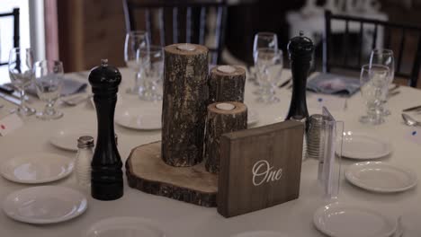 Wedding-reception-venue-rustic-table-décor-and-place-settings,-with-white-dishes,-wood-candles-and-centerpiece-and-white-table-cloth