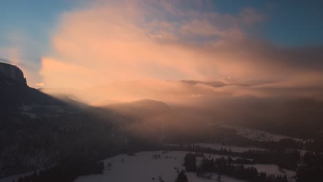 Drone-shot-of-a-mysterious-landscape-at-sunset-in-the-mountains-covered-with-clouds-in-wintertime