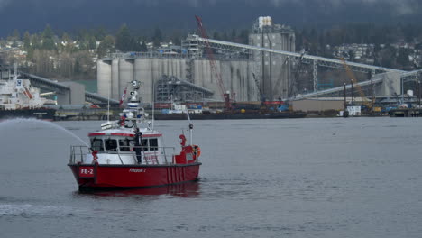 Kanadisches-Feuerlöschboot,-Das-Mit-Wasser-Sprüht,-Trainingsübung-Auf-Dem-Fluss-Mit-Industriefabrik-Im-Hintergrund