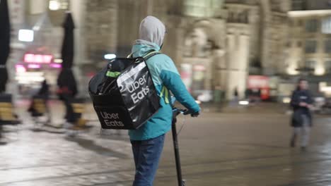 Young-Uber-Eats-courier-delivering-food-to-a-customer-on-the-electric-scooter-in-winter-time
