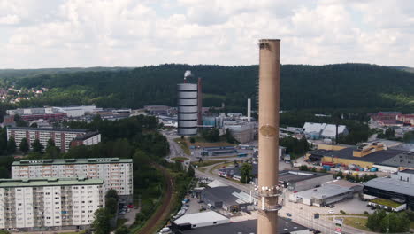 Apartment-buildings-and-massive-industrial-chimney-in-Swedish-city,-aerial-drone-view