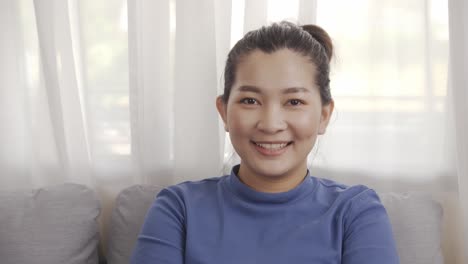 Asiatische-Frau,-Die-Ein-Blaues-Hemd-Trägt,-Das-Auf-Einem-Sofa-Sitzt-Und-Sich-Glücklich-Entspannt