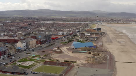 An-aerial-view-of-Rhyl-promenade-and-seafront-on-a-cloudy-day,-flying-over-the-promenade-towards-Kinmel-Bay-while-zooming-in,-North-Wales,-UK