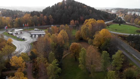 Aerial-Reveal-Of-Gasoline-Station-By-Roadside,-Sweden-Surrounded-By-Trees-In-Autumn-Colors