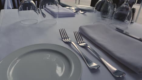 Fine-dining-restaurant-dinner-table-with-settings-on-white-table-cloth-steady-slow-motion-approach-and-tilt-left