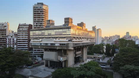 Aerial-dolly-in-of-modern-exposed-concrete-National-Library-between-buildings-and-trees-at-sunset,-Buenos-Aires