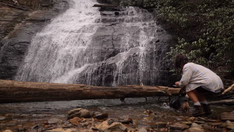 An-owner-and-her-dog-hike-to-a-waterfall-and-take-a-picture---slow-motion-dog-playing-in-water