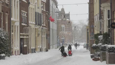 Picturesque-snowing-scene-in-The-Netherlands-with-a-young-family-of-which-the-children-ride-a-sledge-that-their-parents-tow-in-historic-city-centre