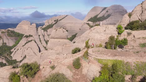 Breathtaking-aerial-view-of-Montserrat-rocky-mountain,-marathon-runners-crossing-paths,-circle-pan,-day