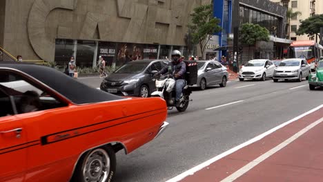 A-1971-orange-Dodge-Dart-driving-on-Paulista-avenue-with-a-motorcycle-behind-it,-close-up-static