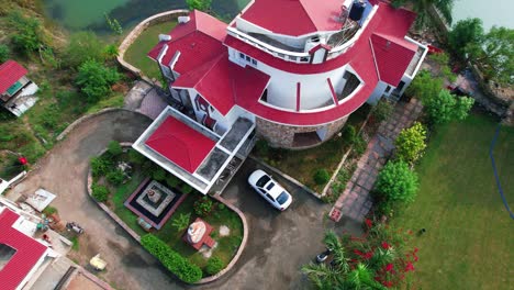White-car-parking-at-the-luxury-house,-aerial-drone-shot-going-up,-with-white-birds-flying-and-luxury-vacation-resort-around-with-swimming-pool-and-lake-in-Vadodara,-India