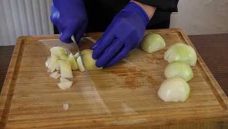 Close-up-professional-chef-heads-wearing-gloves-chopping-onion-on-wooden-cutting-board-in-professional-restaurant-kitchen-food-preparation