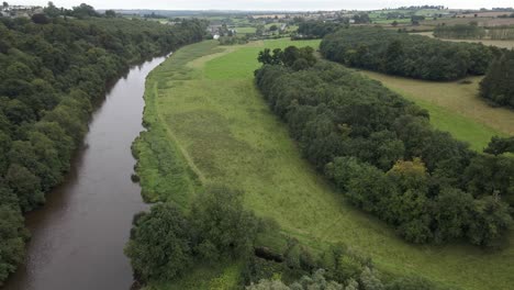 Drone-shot-of-a-large-river-flowing-through-green-fields