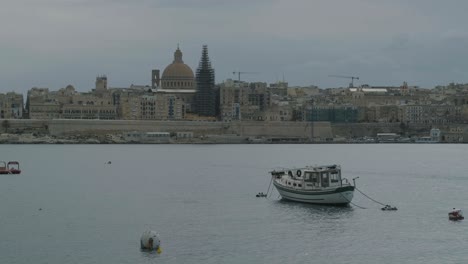 Friedliche-Szene-Eines-Isolierten-Bootes,-Das-Im-Hafen-Von-Valletta-Festgemacht-Ist-Und-Sich-Entlang-Der-Wellen-Bewegt,-Mit-Der-Altstadt-Im-Hintergrund,-Malta