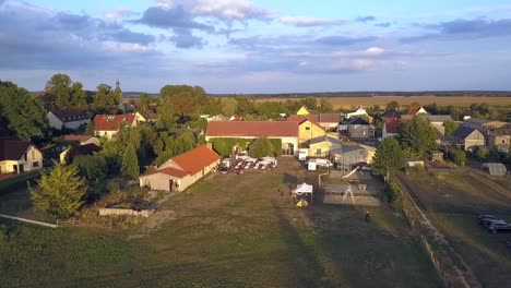 Dramatic-aerial-drone-flight-slowly-sinking-down-drone-shot-of-a-farm-at-summer-sunset-with-long-shadows-on-a-lake-at-small-village-in-Brandenburg-Germany