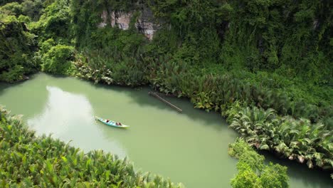 Aerial-view-of-a-local-boat-floating-down-a-green-river-in-Ramang-Ramang-Sulawesi-surrounded-by-jungle,-magroves,-and-palm-trees