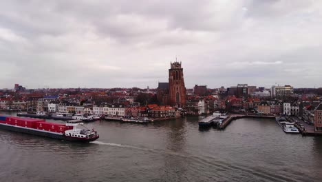 Aerial-Circle-Dolly-View-Of-Cargo-Vessel-Going-Past-On-Oude-Maas-With-Our-Lady-of-Dordrecht-In-Background