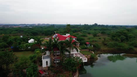 360-degree-aerial-view-of-vacation-house-surrounded-by-a-heavenly-lake,-parking-and-privacy,-with-lake-and-enchanted-green-nature-in-Vadodara,-India