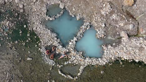 Top-down-View-Of-Tourists-Relaxing-On-Rocky-Shore-of-a-hot-spring-in-jackson,-wyoming---drone-shot