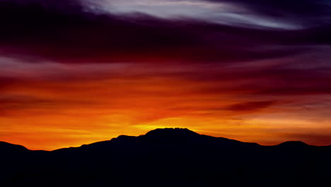 Timelapse-shot-of-beautiful-red-colored-sunrise-behind-mountain-peak-silhouette