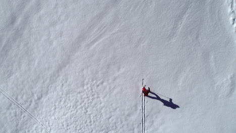 Aerial-top-down-view-of-a-lone-person-skiing-across-a-remote-mountain-peak,-leaving-the-tracks-of-his-adventure-behind