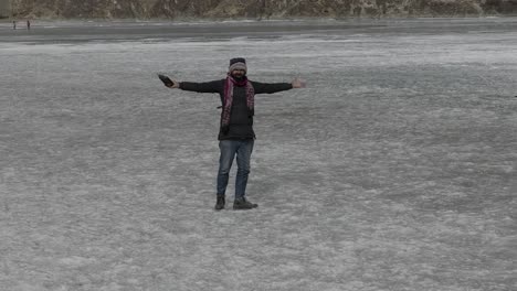 Adult-Male-Walking-Across-Frozen-Lake-Before-Turning-Around-With-Open-Arms-Holding-Drone-Controller