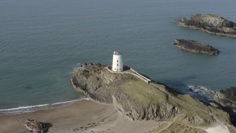 An-aerial-view-of-Twr-Mawr-Lighthouse-on-Ynys-Llanddwyn-island,-flying-right-to-left-around-the-lighthouse-while-zooming-in,-Anglesey,-North-Wales,-UK