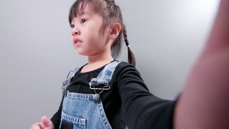 Glückliches-Kleines-Asiatisches-Mädchen,-Das-Ein-Smartphone-Für-Videoanrufe-Nutzt,-Mit-Der-Hand-Winkt-Und-Mit-Einem-Lächeln-Spricht-Und-Spricht-Und-Lehrer-Und-Klassenkameraden-Begrüßt