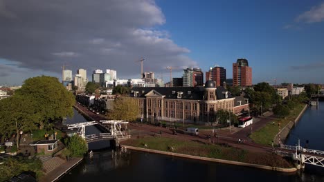 Aufsteigende-Luftaufnahmen,-Die-Das-Muntgebouw-Museum-In-Utrecht-Mit-Einer-Kleinen-Zugbrücke-über-Den-Kanal-Davor-An-Einem-Strahlend-Sonnigen-Tag-Zeigen,-Mit-Dem-Finanzviertel-Im-Hintergrund