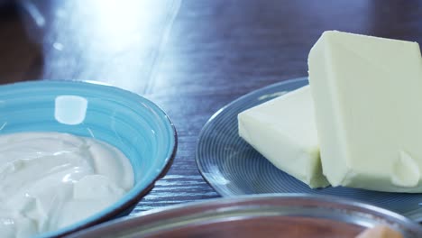 Close-up-of-fresh-healthy-creamy-yogurt-sauce-in-a-bowl-and-cow-butter-cubes-ready-for-tasty-healthy-breakfast
